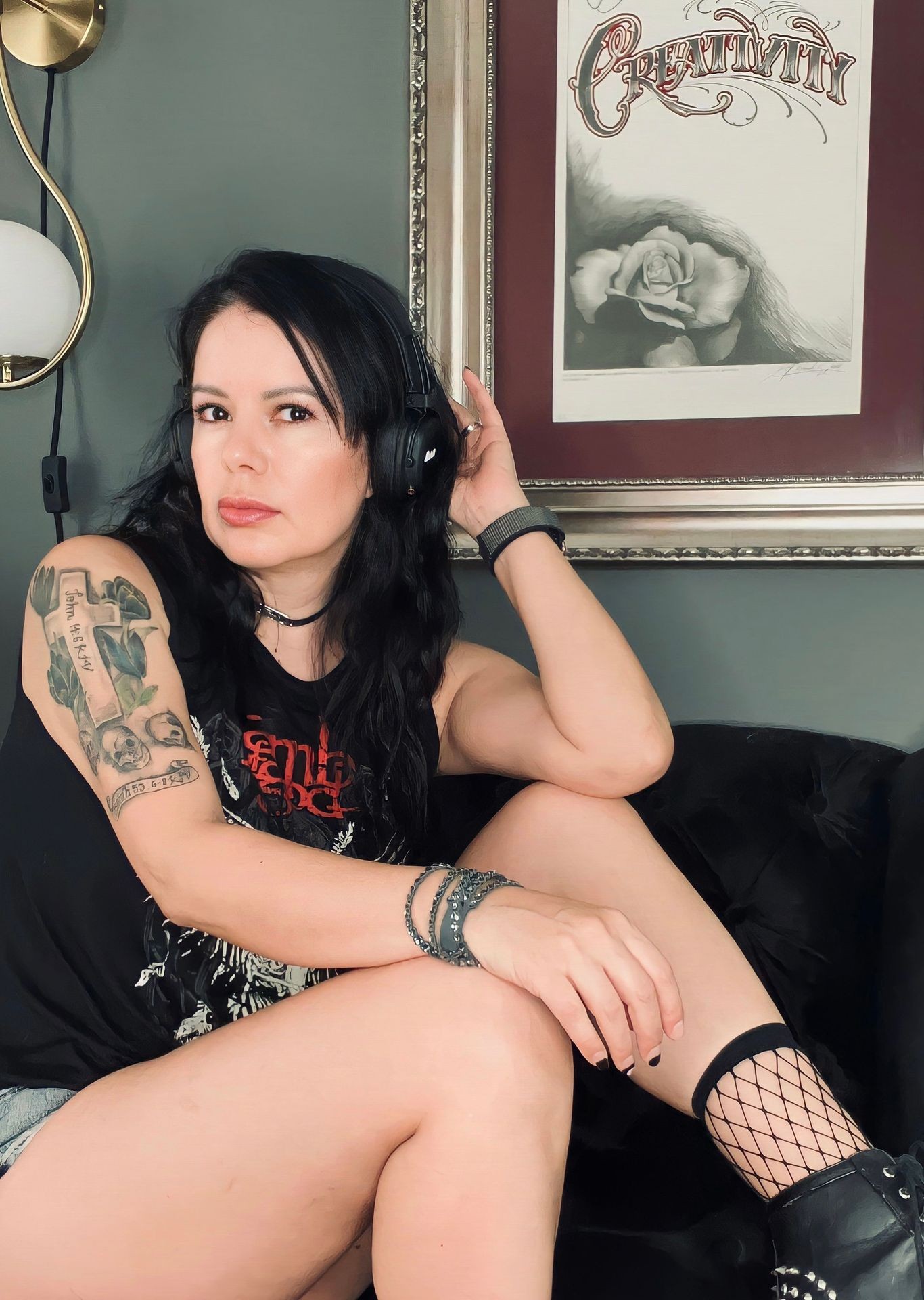 Person in black headphones and tattoo, sitting on a sofa with a framed artwork in the background.